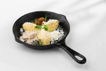 Typical Ukrainian dish polenta - Banosh with cheese, lard and white mushrooms. Maize porridge with bacon, cracklings and cheese. Corn porridge in black pan on white background. Horizontal photo.