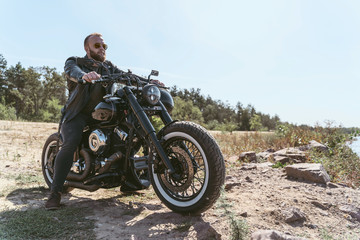 Fototapeta na wymiar Handsome bearded biker in leather jacket sitting on his bike