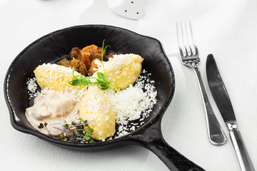 Typical Ukrainian dish polenta - Banosh with cheese, lard and white mushrooms. Maize porridge with bacon, cracklings and cheese. Corn porridge in black pan on white background. Horizontal photo.