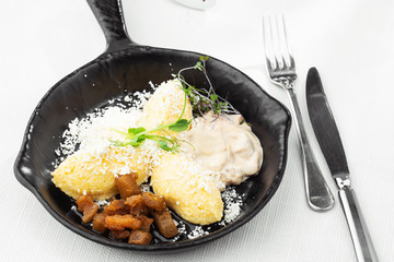 Typical Ukrainian dish polenta - Banosh with cheese, lard and white mushrooms. Maize porridge with bacon, cracklings and cheese. Corn porridge in black pan on white background. Horizontal photo.