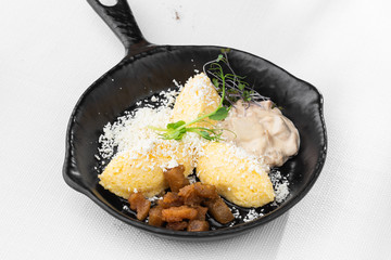 Typical Ukrainian dish polenta - Banosh with cheese, lard and white mushrooms. Maize porridge with bacon, cracklings and cheese. Corn porridge in black pan on white background. Horizontal photo.