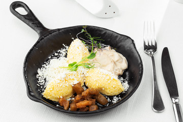 Typical Ukrainian dish polenta - Banosh with cheese, lard and white mushrooms. Maize porridge with bacon, cracklings and cheese. Corn porridge in black pan on white background. Horizontal photo.
