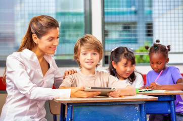 Multi ethnic elementary classroom. Three classmates enjoying school time with teacher