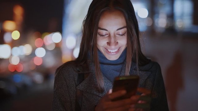 Closeup of prety smiling woman using smartphone walking at night city, slowmotion fullHD stock footage, handheld camera shot