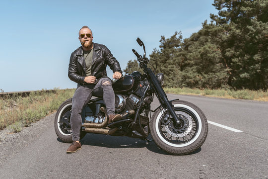 Sexy biker in leather jacket with sigar sitting on his bike on the road