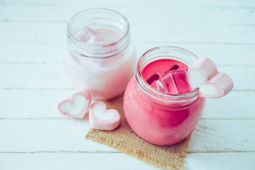 Pink milkshake with heart shape marshmallows on wood background