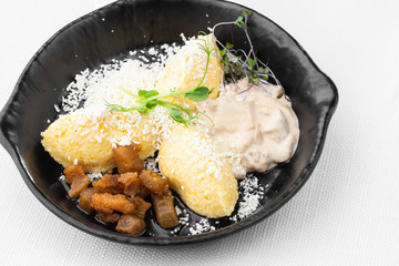 Typical Ukrainian dish polenta - Banosh with cheese, lard and white mushrooms. Maize porridge with bacon, cracklings and cheese. Corn porridge in black pan on white background. Horizontal photo.