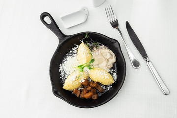 Typical Ukrainian dish polenta - Banosh with cheese, lard and white mushrooms. Maize porridge with bacon, cracklings and cheese. Corn porridge in black pan on white background. Horizontal photo.