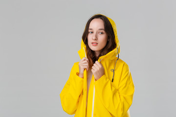 Pretty brunette girl in a yellow raincoat smiling isolated over grey background. Get ready for bad...
