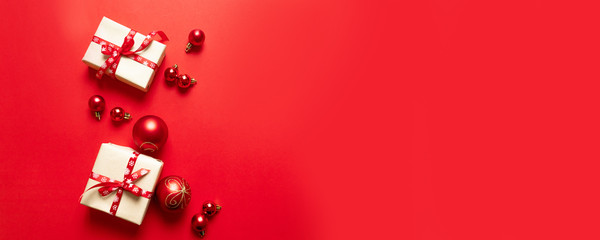 Christmas composition with festive red craft boxes and red ribbons and small balls on red background.