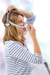 Woman trying to wear CPAP mask, sleep apnea therapy.Profile view - obrazy, fototapety, plakaty