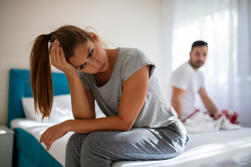 We have a problem. Young upset girl sitting on the edge of the bed, against her boyfriend. Relationship Difficulties: Young couple having problems. Young couple having problems.