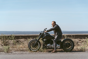 Brutal athletic biker sitting on the motorcycle by the ocean