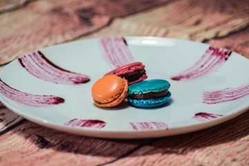 blue, orange and fuchsia macaroons on a white plate with purple stripes on it on a wooden background