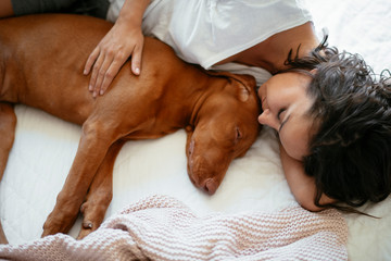 Close up young woman sleeping with dog in bed