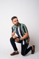 Full body shot of young bearded Indian man crouching and thinking