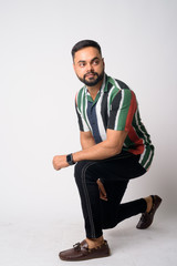 Full body shot of young bearded Indian man crouching and thinking