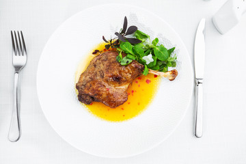 Roast duck leg with mango sauce, salade and chilli pepper on white plate, closeup. Horizontal view from above, top shot. White background.