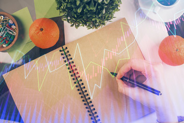 Forex chart hologram on hand taking notes background. Concept of analysis. Double exposure