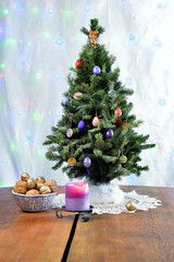 Christmas tree with a candle and a bowl of walnuts on the wooden table