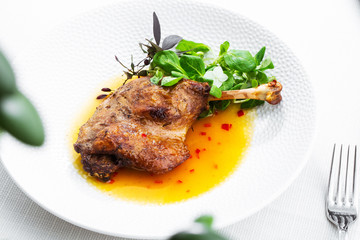 Roast duck leg with mango sauce, salade and chilli pepper on white plate, closeup. Horizontal view from above, top shot. White background.