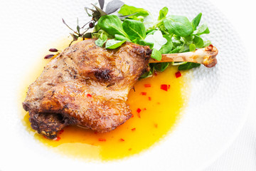 Roast duck leg with mango sauce, salade and chilli pepper on white plate, closeup. Horizontal view from above, top shot. White background.