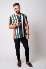 Full body shot of young bearded Indian man using phone