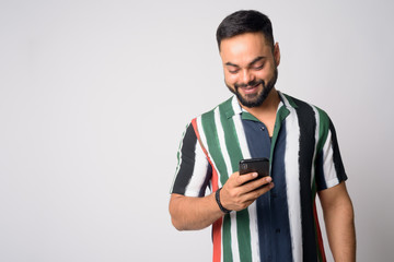 Portrait of happy young bearded Indian man using phone
