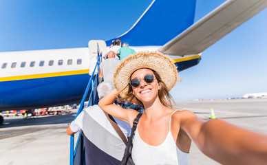 Young woman takes a selfie at the airport in front of a plane before the departure. Concept about...