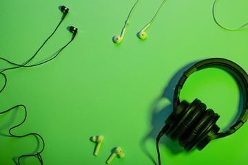 Headphones of different types flat lay on green color background, copy space. Black in ear headphones, wireless and foldable over ear headphones closeup with cable, music concept, top view.