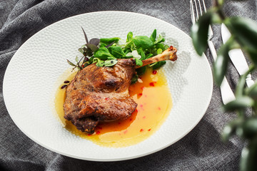 Roast duck leg with mango sauce, salade and chilli pepper on white plate, closeup. Horizontal view from above, top shot. Gray background.