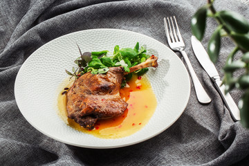 Roast duck leg with mango sauce, salade and chilli pepper on white plate, closeup. Horizontal view from above, top shot. Gray background.