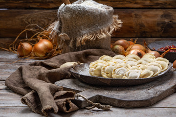 uncooked meat dumplings - russian pelmeni on cutting board and ingredients for homemade pelmeni on wooden table. Process of making pelmeni, ravioli or dumplings with meat