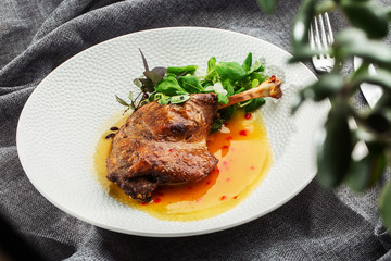 Roast duck leg with mango sauce, salade and chilli pepper on white plate, closeup. Horizontal view from above, top shot. Gray background.