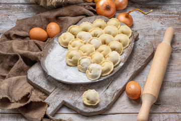 uncooked meat dumplings - russian pelmeni on cutting board and ingredients for homemade pelmeni on wooden table. Process of making pelmeni, ravioli or dumplings with meat
