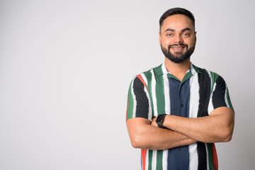 Portrait of happy young bearded Indian man smiling with arms crossed