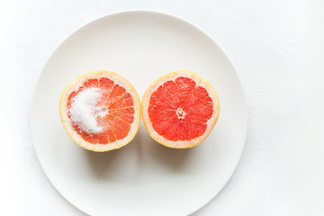 Fototapeta na wymiar Half a grapefruit with sugar on a white plate on a light background