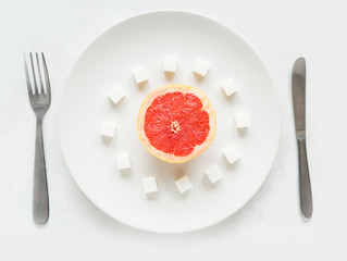Half a grapefruit with sugar refined sugar on a white plate on a light background