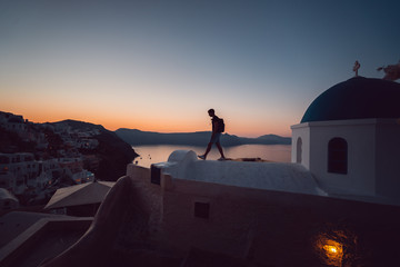 Man walking on top of a Church at sunrise with the Santorini Caldera in the distant background....
