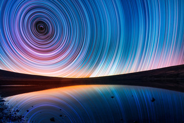 Beautiful night landscape, old volcano, crater lake. The colorful star trails on the sky. Night timelapse photography.