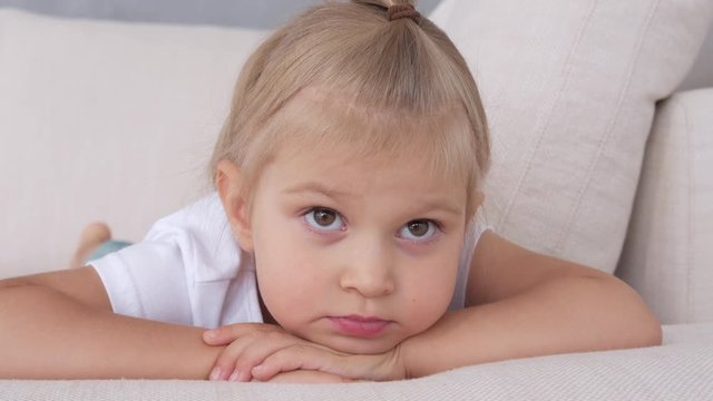 A little girl is lying on a soft couch looking at the TV screen.