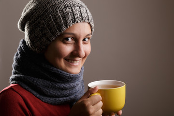 Young woman wearing a woolen scarf and a cap drinking hot tea. Autumn and winter season and illness concept.