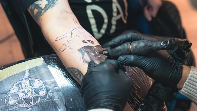 Professional tattoo artist makes a tattoo on a young man’s hand, close-up. Tattoo artist doing tattoo in tattoo salon.