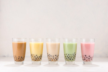 Row of fresh boba bubble tea glasses on white background.