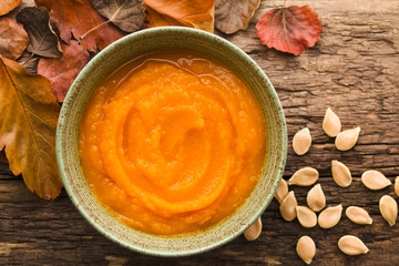 Fresh homemade pumpkin puree in bowl, colorful autumn leaves and pumpkin seeds on the side, photographed overhead (Selective Focus, Focus on the dish)