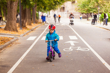 Happy boy of three years riding on balance bike in autumn