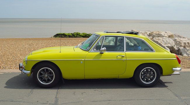  Classic Yellow MGB GT parked on seafront promenade.