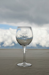 Empty transparent glass on beige table, in which reflected white clouds