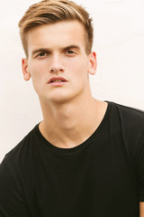 Obraz premium Portrait of a stylish young blond man in a black t-shirt on a white background.