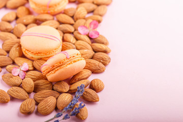 Orange macarons or macaroons cakes with almond nuts on pastel pink background. side view, copy space.